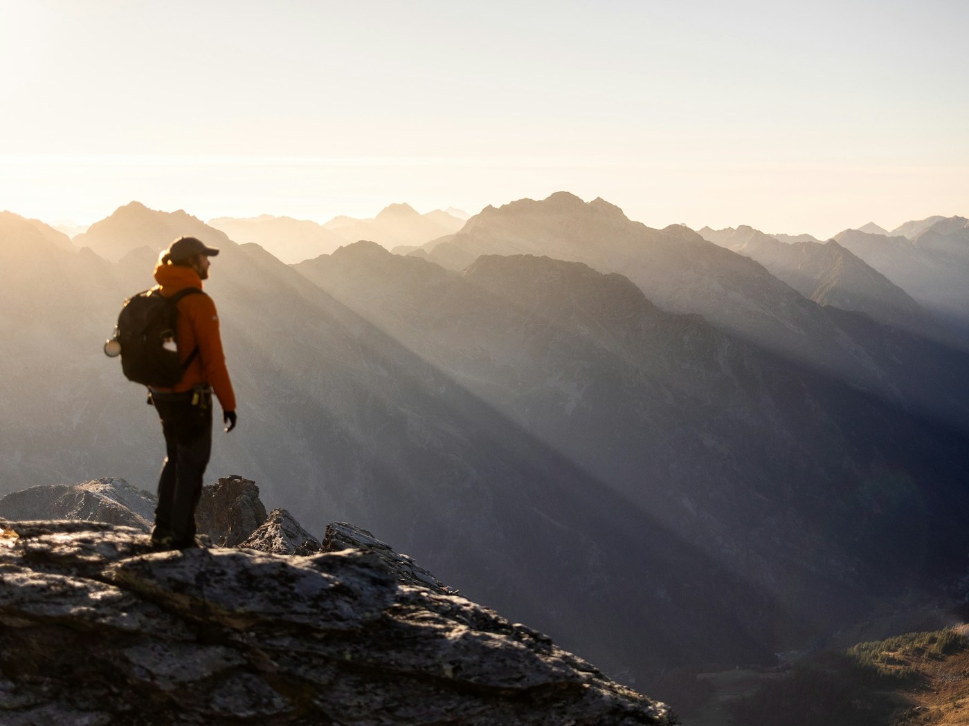 Hiker on a mountain peak at sunrise overlooking the valley below